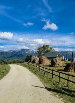 A panoramic view of green fields with haystacks and a path leading to high mo Stock Photos