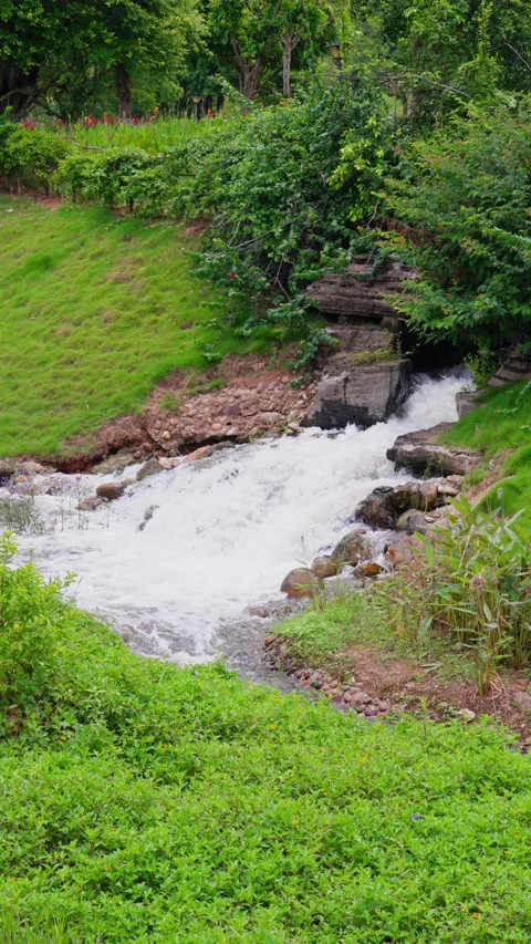 Panoramic view of green grassy slope surrounded by rocky stream falling water Stock Footage 340485995