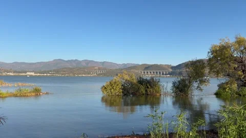 Panoramic view of lake, mountains, wind turbines in golden hour light Stock Footage 323525837