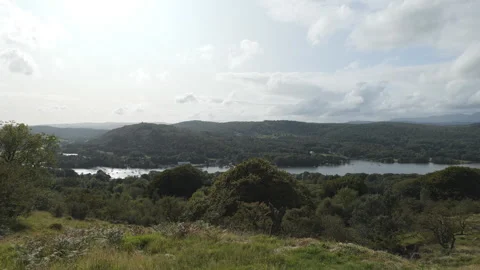 A panoramic view of a lake surrounded by wooded hills under a partly cloudy sky. Stock Footage 313770470