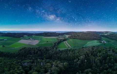 Panoramic view of lush fields and forests under a starlit sky at twilight i.. Stock Photos