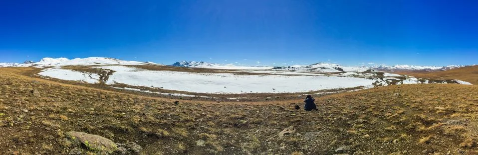 Panoramic view of a man sitting alone at the Deosai plains national park. Stock Photos
