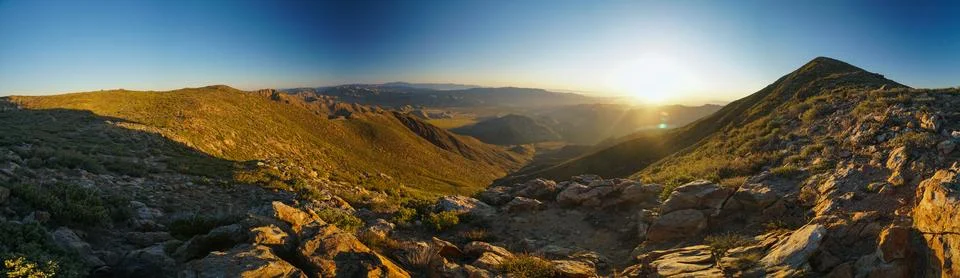 A panoramic view of a mountain range with a sun setting in the background Stock Photos