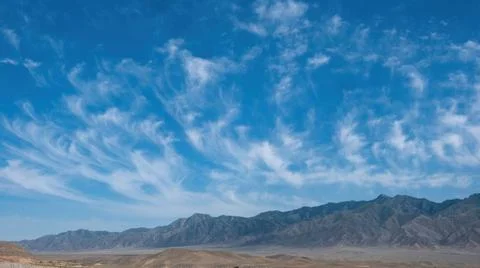 Panoramic view of a mountain range under a wide blue sky with wispy cirrus cl Stock Photos