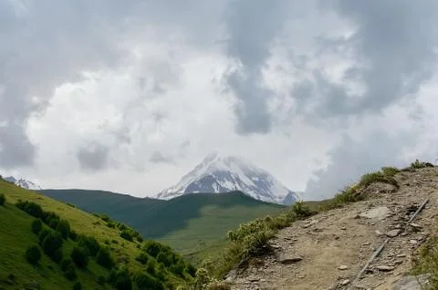Panoramic view from a mountainous rocky path to a huge snow-capped peak in th Stockfoto's