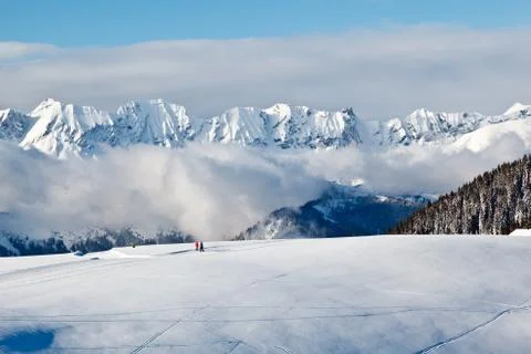 Panoramic view on mountains and two people trekking in french alps in winter Stock Photos