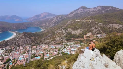 Panoramic view of Oludeniz beach with man sit on the rock shooting himself drone Stock Footage 226154928