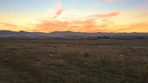 Panoramic view of open countryside beneath a glowing sunset, with snow-dusted Stock Footage 345254351