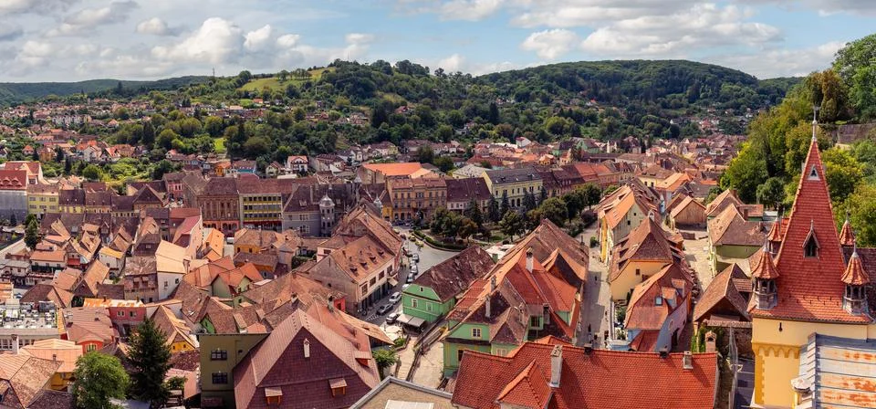 Panoramic view over red tiled rooftops and green hills of historic Sighisoara 库存照片