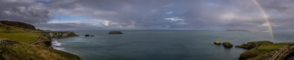 Panoramic view of a rainbow shining between rainy clouds, sea and cliffs near Stock Photos