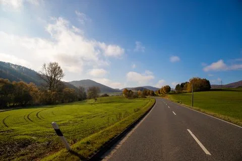 Panoramic view on a road with green meadows blue sky, in autumn with forest Stock Photos