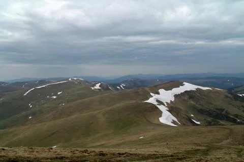 Panoramic view of rolling mountain ridges with snow patches under a cloudy ov Stock Photos