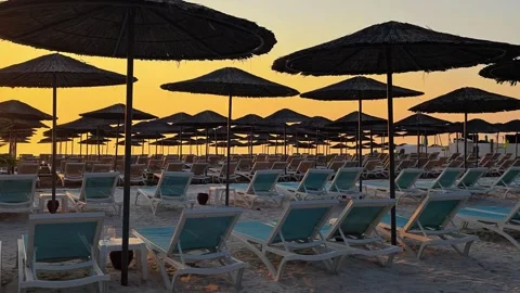 Panoramic view row of silhouettes umbrellas and empty sun loungers at sunset. Stock Footage 313136983