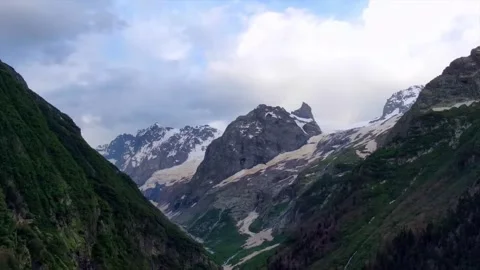 Panoramic view of rugged snow covered mountain peaks under a cloudy summer sky 库存影片 338241000