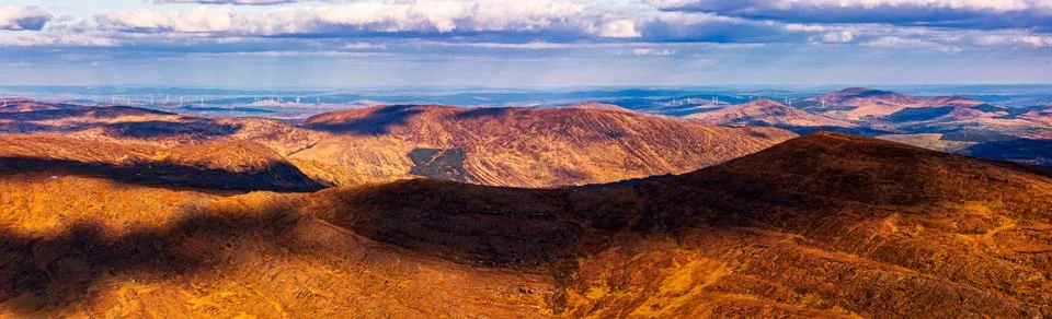 A panoramic view shows rolling hills covered in vegetation, with shadows Stock Photos