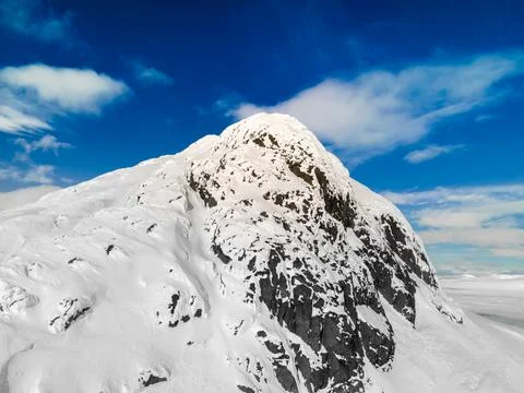 Panoramic view of a snow capped mountain peak with clouds and blue skies. Stock Photos
