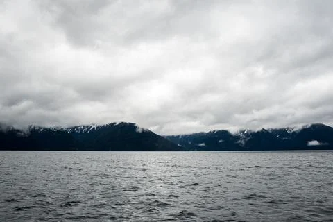 Panoramic view of snow-capped mountains on a cloudy day and a lake on the bot Stock Photos