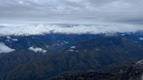 Panoramic View of Snow-Capped Mountains Above Forest Valley Under Cloudy Sky Stock Photos