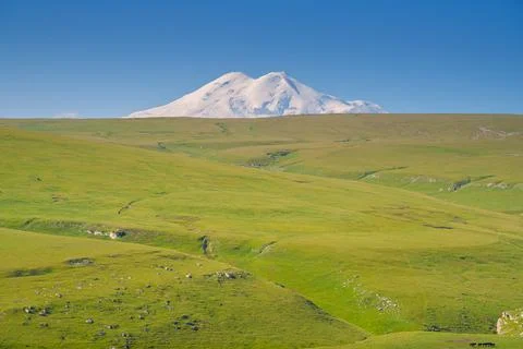 A panoramic view of the snow-capped peaks of Mount Elbrus with the green fiel Stock Photos