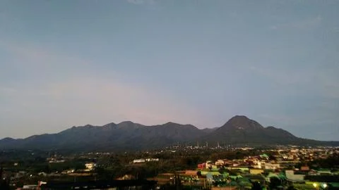 Panoramic view of a town nestled at the base of lush green mountains at dusk Stock Photos
