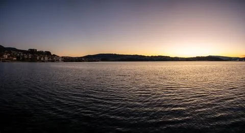 Panoramic view of a tranquil lake at sunset with silhouettes of distant hil.. Stock Photos