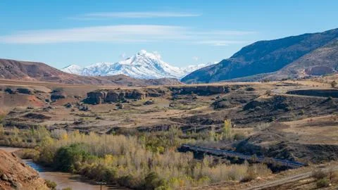 Panoramic view of a valley with a train and railway with snow capped mountain Stock-Fotos