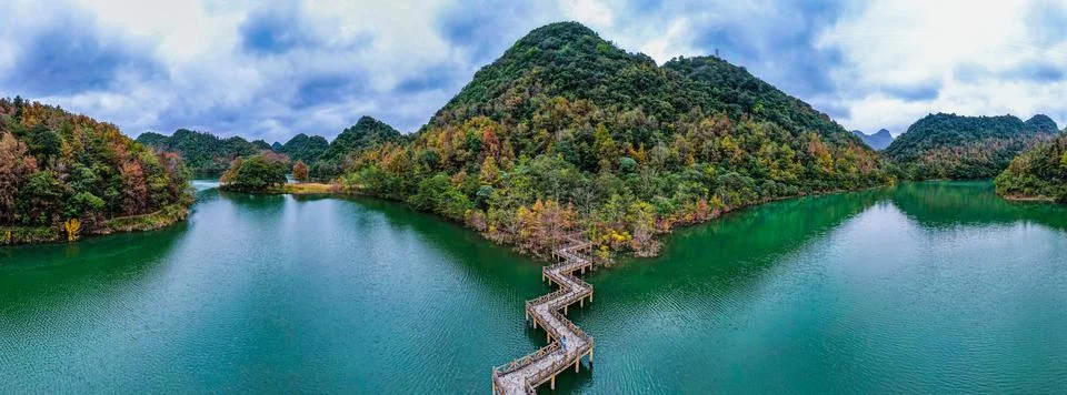 Panoramic view of a zig-zag bridge over the lake surrounded by tree-covered hill 스톡 사진
