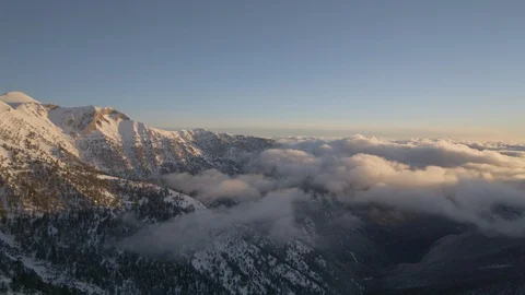 Panoramic wide shot of clouds rolling over snowy mountains at sunset Stock Footage 113222276