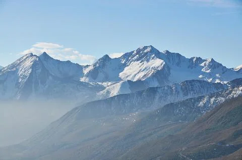 A panoramic winter view of snow-covered mountain peaks under a cold, white sky Stock Photos