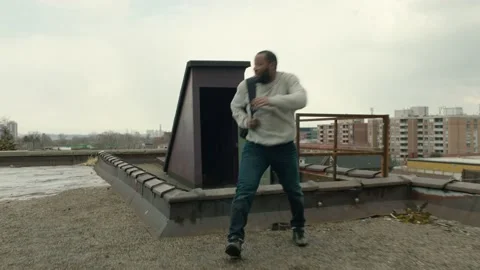 Panting man runs out through a door to a warehouse rooftop, catches his breath a Stock Footage 199461650