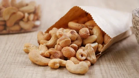 A paper bag filled with cashews tips over, and the nuts scatter across the table Stock Footage 345293624
