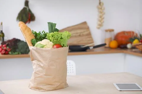 Paper bag full of vegetables on the table in kitchen interiors. Healthy meal and Stock-Fotos