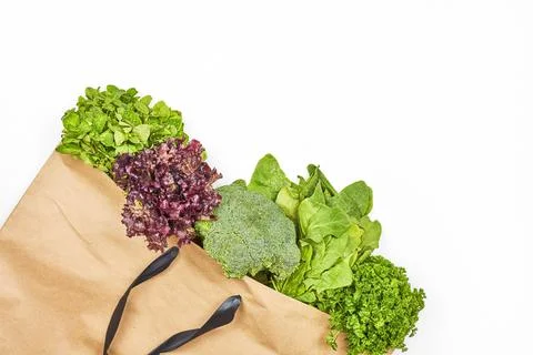 Paper bag with green leafy vegetables salad on white background Stock Photos
