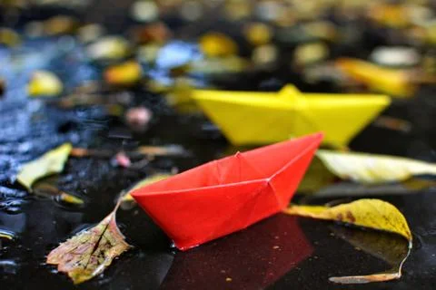 Paper boat float in puddle on surface of wet asphalt Stock Photos