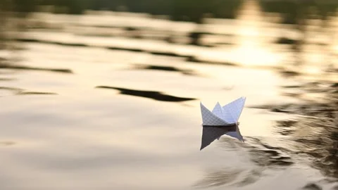 A paper boat is floating on the waves in the water at a beautiful sunset. Vidéo 200560373
