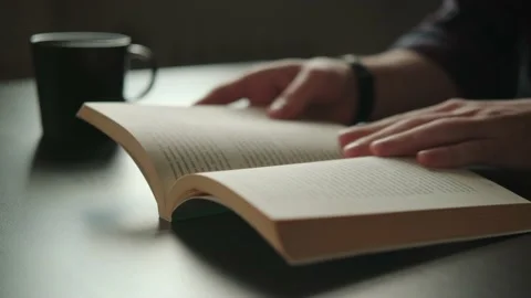 Paper book and coffee on the table, man reads, turns a page 库存影片 162214650