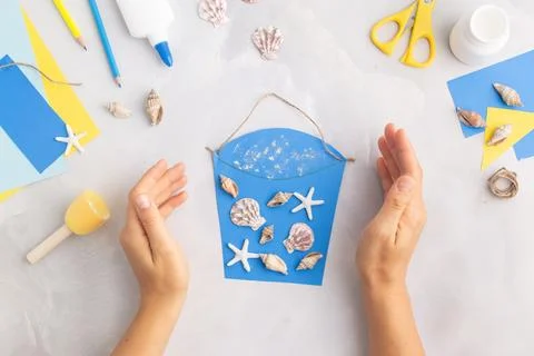 Paper bucket of shells summer idea for kids craft in kindergarten hands ocean's Stock Photos