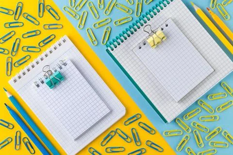 Paper clips and Notepad on bright yellow and blue paper background. Stock Photos