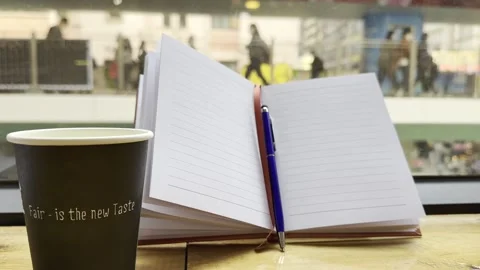 Paper coffee cup next to an open lined notebook and pen on a wooden table Stock Footage 297717240