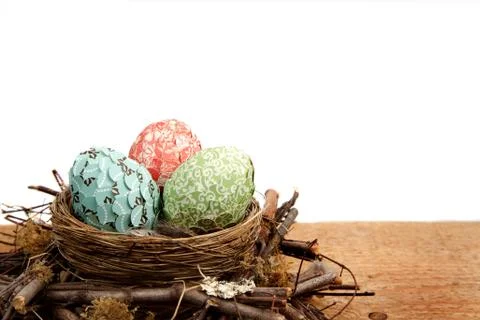 Paper covered easter eggs in a nest on a white background Stock Photos