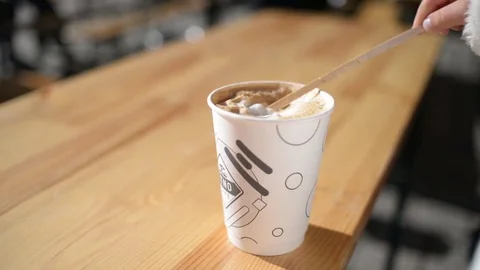A paper Cup of Cappuccino - a child eats Foam with a sStick Video stock 80859798