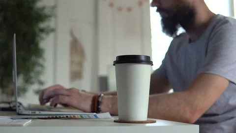 Paper Cup closeup. Young man working on computer and drinking coffee Stock Footage 83783328