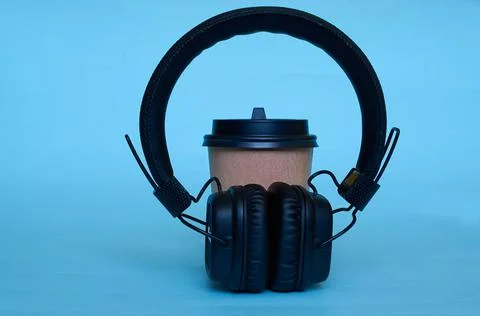 A paper cup for coffee and wireless headphones on a blue background. Stock Photos
