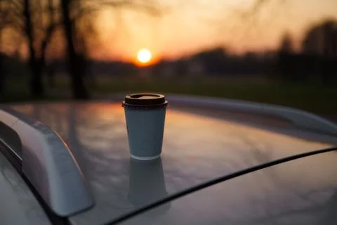 Paper cup coffee at sunset standing on a car roof with beautiful out of focus Stock Photos