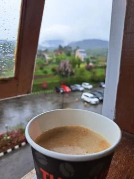 A Paper Cup of Hot Coffee by Window Overlooking Misty Mountains and Rainy Garden Stock Photos