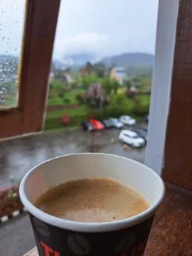 A Paper Cup of Hot Coffee by Window Overlooking Misty Mountains and Rainy Garden Stock Photos