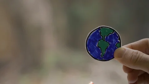 Paper drawing of earth held by hand being burnt with a match. Global Stock Footage 121531993