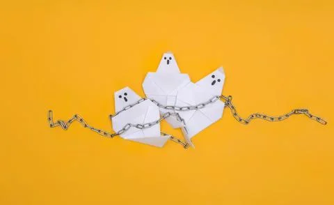 Paper ghost figures chained together on yellow background Stock Photos