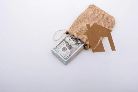 Paper house placed beside a bundle of US dollar banknote Stock Photos
