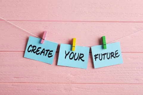 Paper notes with motivational phrase Create Your Future hanging on pink woo.. Stock Photos